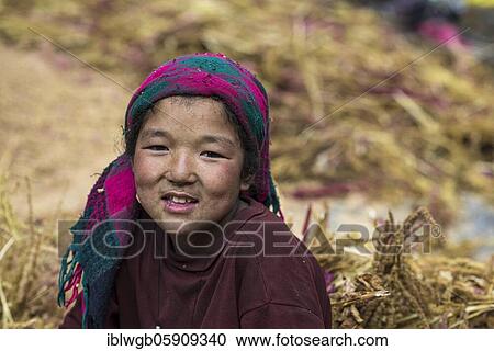 Stock Image - A little girl sitting in a pile of pearl millet, Manaslu region, Himalayas, Nepal, Asia. Fotosearch