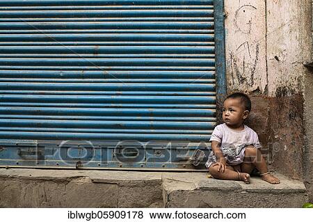 Stock Photo - A little girl sitting in front of a rolling gate, Kathmandu, Nepal, Asia. Fotosearch