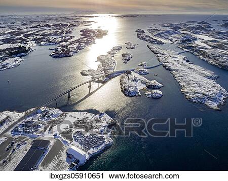 Stock Image - Aerial view, country road with bridge over the sea connects populated, small, winterly islands with the mainland, behind mountains, Herøy, Nordland, Norway, Europe. Fotosearch