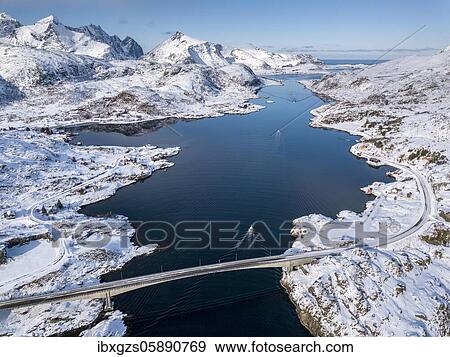 Stock Photo - Aerial view, Fjord seaway with snowy mountains, bridge with road and small fishing boats, Nordland, Lofoten, Norway, Europe. Fotosearch