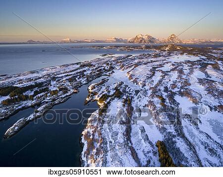 Stock Image - Aerial view of winter island landscape in the evening light off the coast, high mountain peaks in the background, Dønna, Nordland, Norway, Europe. Fotosearch