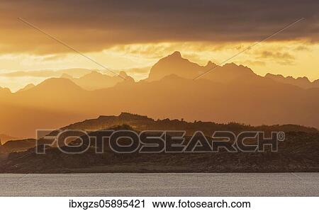 Stock Image - Atmospheric sunset over a high mountain range, in front sea, Bodø, Nordland, Norway, Europe. Fotosearch