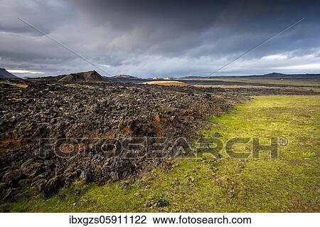 Stock Image - Black solidified lava borders on lush green grass with dramatic clouds in Leihrnjukur in Krafla, Skútustaðir, Norðurland eystra, Iceland, Europe. Fotosearch