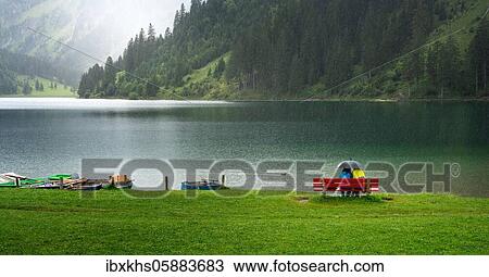 Stock Image - Couple with umbrella sitting in the rain at Vilsalpsee in Tyrol, Austria, Europe. Fotosearch