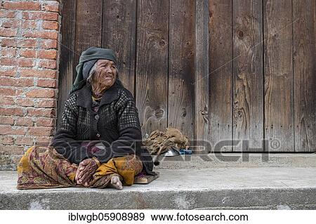 Stock Photo - Elderly woman with headscarf and nose ring sitting in front of a wooden door, Himalaya, Jiri, Khumbu region, Nepal, Asia. Fotosearch