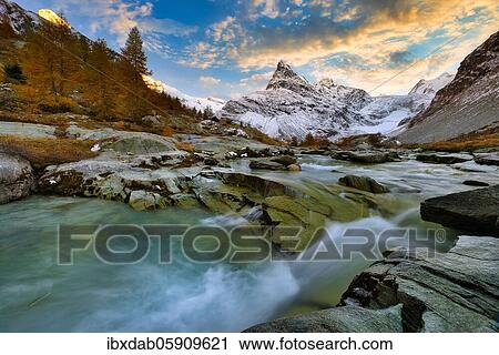 Stock Image - Evening mood at the brook near Ferpècle, behind it snowy Mont Miné, Val d'Hérens, Canton Valais, Switzerland, Europe. Fotosearch