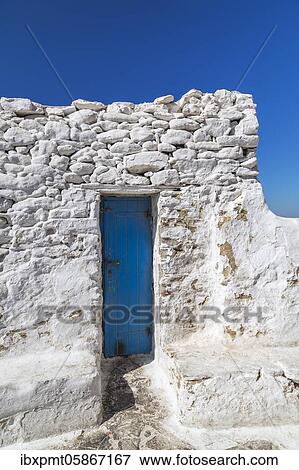 Stock Photo - Exposed white painted stone building wall with narrow blue painted front entrance door, Mykonos Town, Mykonos Island, Greece, Europe. Fotosearch