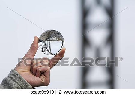 Stock Image - Hand holding glass ball, Old Harburg Elbe bridge is reflected in it, Harburg, Hamburg, Germany, Europe. Fotosearch