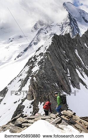 Stock Image - Hiker at the rugged mountain peak, Schönbichler Horn, Großer Möseler with Furtschaglkees glacier, snow-covered mountains, high alpine landscape in fog, Berliner Höhenweg, Zillertal Alps, Zillertal, Tyrol, Austria, Europe. Fotosearch