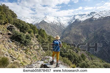 Stock Photo - Hiker on a hiking trail, hiking trail Vereda de la Estrella, behind Sierra Nevada with summits Mulhacén and Pico Alcazaba, snow-covered mountains near Granada, Andalusia, Spain, Europe. Fotosearch