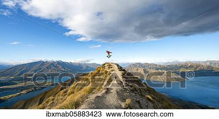 Stock Image - Hiker takes a skydive, views of mountains and lake from Mount Roy, Roys Peak, Lake Wanaka, Southern Alps, Otago, South Island, New Zealand, Oceania. Fotosearch