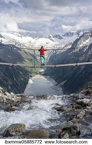 Stock Image - Hiker, woman on suspension bridge at the Olpererhütte, Schlegeis reservoir, Schlegeis reservoir, Zillertal Alps, Schlegeiskees glacier, Zillertal, Tyrol, Austria, Europe. Fotosearch
