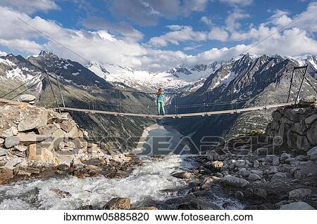 Stock Image - Hiker, woman on suspension bridge at the Olpererhütte, Schlegeis reservoir, Schlegeis reservoir, Zillertal Alps, Schlegeiskees glacier, Zillertal, Tyrol, Austria, Europe. Fotosearch