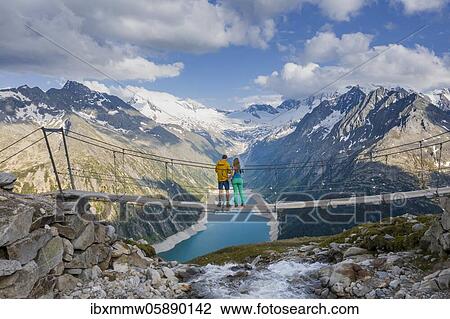 Hiker, young woman and young man on a suspension bridge at the Olpererhütte, view of the Schlegeis reservoir, Schlegeis reservoir, behind the Zillertal Alps with Schlegeiskees glacier, Zillertal, Tyrol, Austria, Europe View Large Photo Image Stock Image - Hiker, young woman and young man on a suspension bridge at the Olpererhütte, view of the Schlegeis reservoir, Schlegeis reservoir, behind the Zillertal Alps with Schlegeiskees glacier, Zillertal, Tyrol, Austria, Europe. Fotosearch