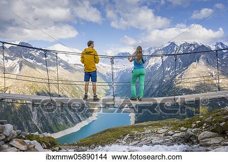 Picture - Hiker, young woman and young man on suspension bridge at the Olpererhütte, Schlegeis reservoir, Schlegeis reservoir, Zillertal Alps, Schlegeiskees glacier, Zillertal, Tyrol, Austria, Europe. Fotosearch