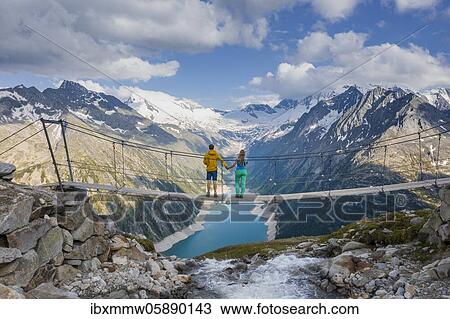 Hiker, young woman and young man on suspension bridge at the Olpererhütte, Schlegeis reservoir, Schlegeis reservoir, Zillertal Alps, Schlegeiskees glacier, Zillertal, Tyrol, Austria, Europe View Large Photo Image Stock Image - Hiker, young woman and young man on suspension bridge at the Olpererhütte, Schlegeis reservoir, Schlegeis reservoir, Zillertal Alps, Schlegeiskees glacier, Zillertal, Tyrol, Austria, Europe. Fotosearch