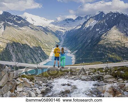 Stock Photograph - Hiker, young woman and young man on suspension bridge at the Olpererhütte, Schlegeis reservoir, Schlegeis reservoir, Zillertal Alps, Schlegeiskees glacier, Zillertal, Tyrol, Austria, Europe. Fotosearch