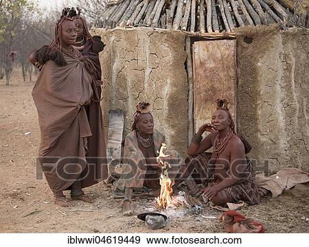 Stock Photo - Himba women sit early in the morning in front of the mud hut at the burning fire, Kaokoveld, Kunene, Namibia, Africa. Fotosearch