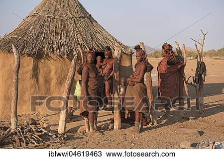 Stock Image - Himba women with small children in front of their hut, Kaokoveld, Namibia, Africa. Fotosearch