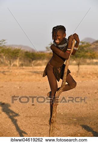 Stock Image - Himbamädchen climbs on a dry tree, Kunene, Kaokoveld, Namibia, Africa. Fotosearch