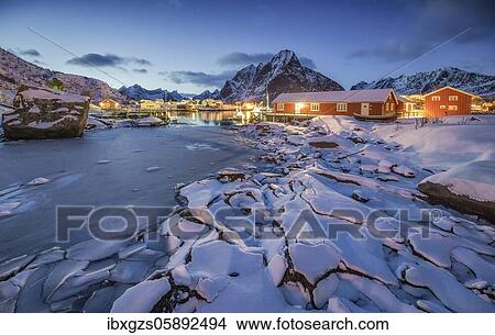 Picture - Ice floes at the frozen fjord, behind red wooden houses and winterly mountain landscape at dusk, Reine, Nordland, Lofoten, Norway, Europe. Fotosearch
