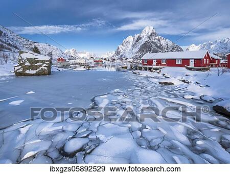 Stock Photo - Ice floes in the frozen fjord, behind red wooden houses and winter mountain scenery, Nordland, Lofoten, Norway, Europe. Fotosearch