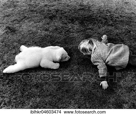 Picture - Little polar bear and a girl lying on the meadow, England, Great Britain. Fotosearch
