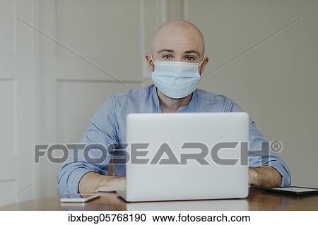 Stock Image - Man with face mask at home office. Fotosearch