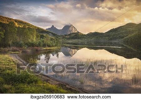 Stock Image - Mist over the lake Agvatnet, wooded hills and mountain tops play in the evening light, Ågskardet, Nordland, Norway, Europe. Fotosearch