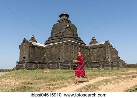 Stock Image - Novice Buddhist monk collects morning alms in front of Laymyetnha Paya, Lemyethna Temple, Mrauk U, Burma, Myanmar, Asia. Fotosearch
