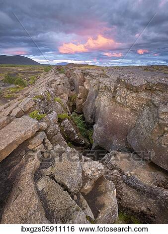 Stock Photograph - Red column in the plain with dramatic clouds in the evening sky in the fault zone, Grjotagjá, Skútustaðir, Norðurland eystra, Iceland, Europe. Fotosearch