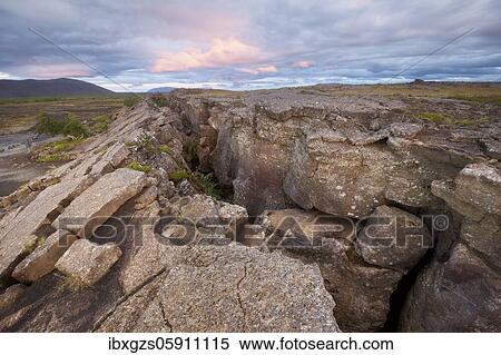 Stock Photography - Red column in the plain with dramatic clouds in the evening sky in the fault zone, Grjotagjá, Skútustaðir, Norðurland eystra, Iceland, Europe. Fotosearch