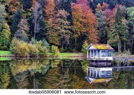 Stock Image - Reflection of the boathouse on the Wenigerweier, behind it autumn coloured trees, St. Gallen, Canton St. Gallen, Switzerland, Europe. Fotosearch