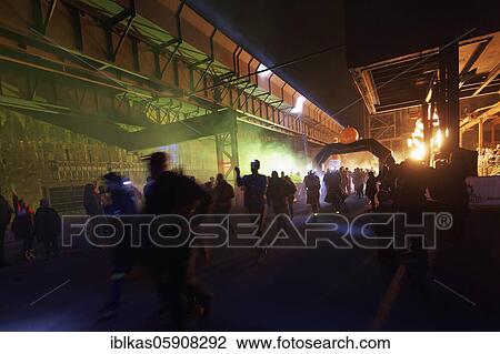Stock Image - Runners in front of an illuminated industrial scenery, Halloween Run in the Landschaftspark Duisburg-Nord, Duisburg-Meiderich, North Rhine-Westphalia, Germany, Europe. Fotosearch