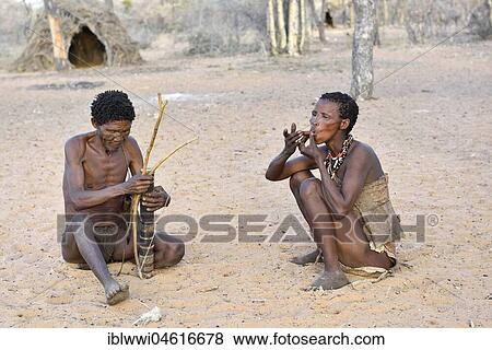 Stock Photo - San man with bow and arrow and smoking woman, Bushman tribe, Kalahari, Namibia, Africa. Fotosearch