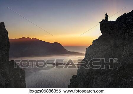 Silhouette of a woman sitting on a rocky outcrop at sunset, in the back sea, fjord and mountains with ground fog, Gimsøy, Lofoten, Nordland, Norway, Europe View Large Photo Image Stock Photography - Silhouette of a woman sitting on a rocky outcrop at sunset, in the back sea, fjord and mountains with ground fog, Gimsøy, Lofoten, Nordland, Norway, Europe. Fotosearch