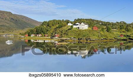 Stock Image - Small settlement, mirrored on a fjord, in the background a fell with wooded mountain slopes, Reipå, Nordland, Norway, Europe. Fotosearch
