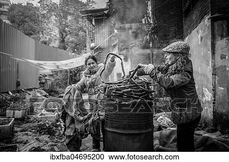 Stock Image - Street scene in an old town quarter of Chongqing. Women are smoking homemade sausages. These districts are gradually being demolished to make room for new residential areas with high-rise buildings, Chongqing, China, Asia. Fotosearch