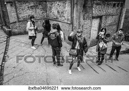 Stock Image - Street scene in an old town quarter of Chongqing. Students photograph scenes from a popular television series. These neighborhoods are gradually being demolished to make room for new residential areas with high-rise buildings, Chongqing, China, Asia. Fotosearch
