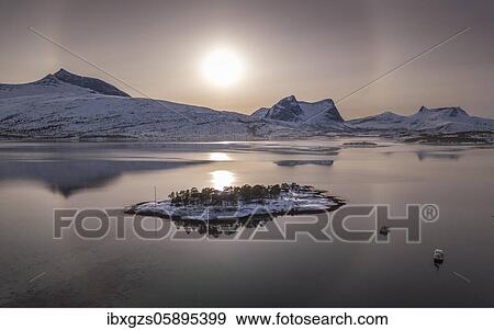 Stock Photo - Sun ring, halo over snowy mountain range, arctic winter landscape, in front small island and fishing boats in a fjord, Ballangen, Nordland, Norway, Europe. Fotosearch