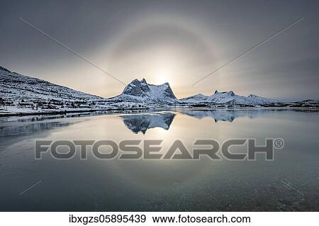 Stock Photo - Sun ring, halo over snowy mountain range Kulhornet, arctic winter landscape, Kobbenestinden, in front sea, Ballangen, Nordland, Norway, Europe. Fotosearch