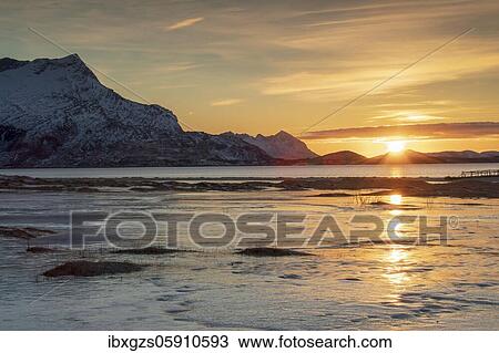 Stock Image - Sunset at sandy beach covered with ice, mountains in the back, Langsanden Strand, Nordland, Norway, Europe. Fotosearch