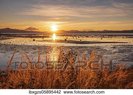 Stock Image - Sunset over a fjord, mountain range in the back, warm evening light, Mo i Rana, Nordland, Norway, Europe. Fotosearch