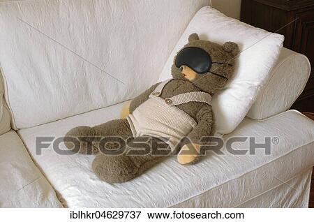 Stock Photo - Teddy Bear lies with a sleeping mask on a couch, Germany, Europe. Fotosearch
