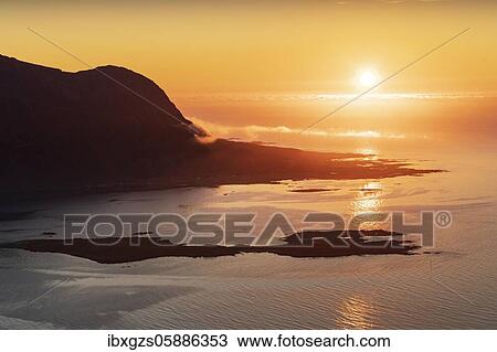 View from the top of Hoven into the sunset, in the back silhouette of a mountain in the sea, Vågan, Lofoten, Nordland, Norway, Europe View Large Photo Image Stock Image - View from the top of Hoven into the sunset, in the back silhouette of a mountain in the sea, Vågan, Lofoten, Nordland, Norway, Europe. Fotosearch