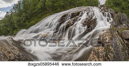 Stock Photograph - Wide waterfall flows over rocks in the forest, Nordland, Norway, Europe. Fotosearch