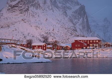 Stock Image - Winter atmosphere early in the morning in the fishing village, stockfish racks, snowfall in the mountains, Reine, Nordland, Lofoten, Norway, Europe. Fotosearch