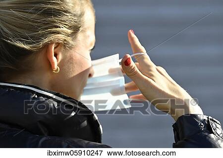 Stock Photo - Woman putting on a face mask, portrait, corona crisis, Stuttgart, Baden-Württemberg, Germany, Europe. Fotosearch