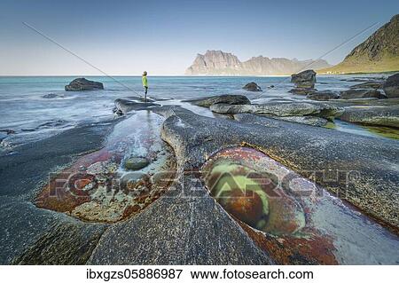 Stock Photo - Woman standing on rocks on the beach, in front tide pool with formation Eye of Utakleiv, Vestvågøy, Nordland, Lofoten, Norway, Europe. Fotosearch