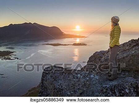 Woman standing on top of Hoven at sunset, behind sea and fjord, Vågan, Lofoten, Nordland, Norway, Europe View Large Photo Image Stock Photo - Woman standing on top of Hoven at sunset, behind sea and fjord, Vågan, Lofoten, Nordland, Norway, Europe. Fotosearch